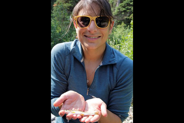 Woman in yellow sunglasses holds small fish, while smiling at the camera
