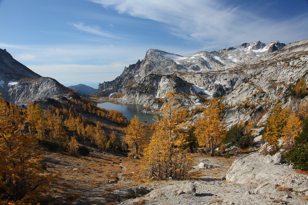 Alpine lake in cirque dotted with aspen trees in full autumn color and surrounded by high mountain peaks dusted with snow