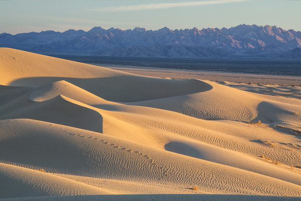 Sand dunes lit by low-angle light glow are flanked by jagged mountains in the distance.