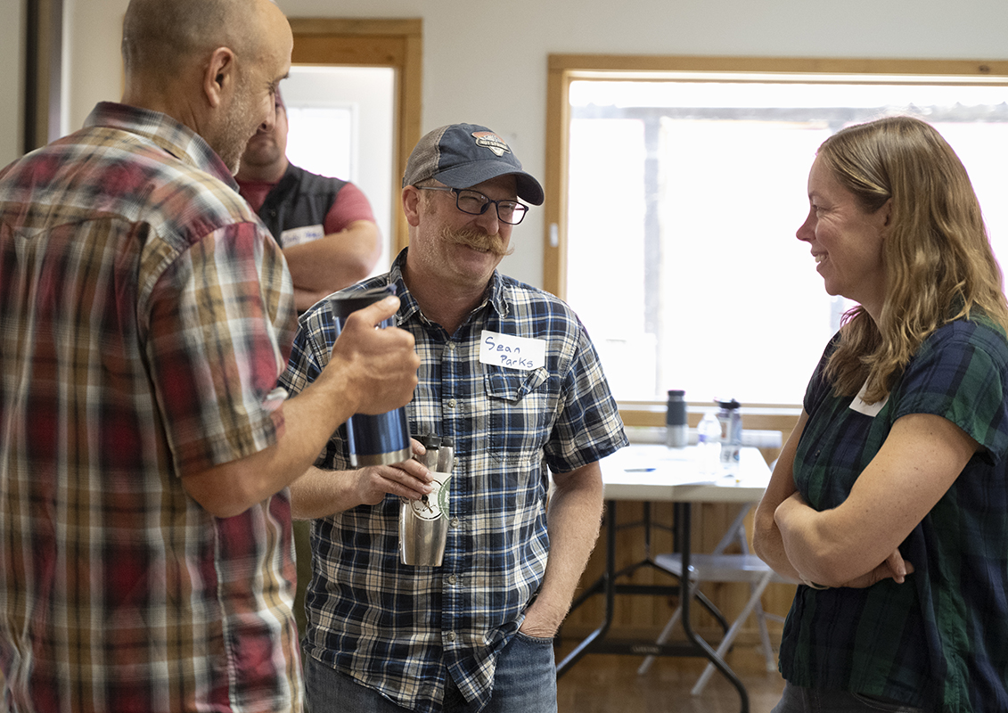 Mustachioed man laughs with two colleagues, a man and a woman.