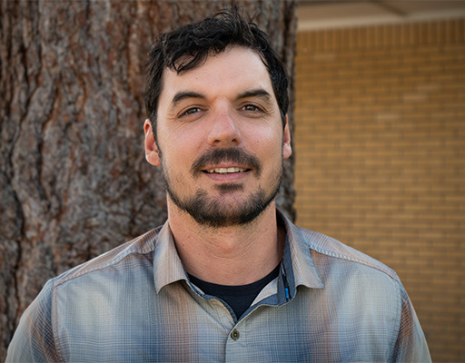 Head shot of man with black hair, smiling at the camera.