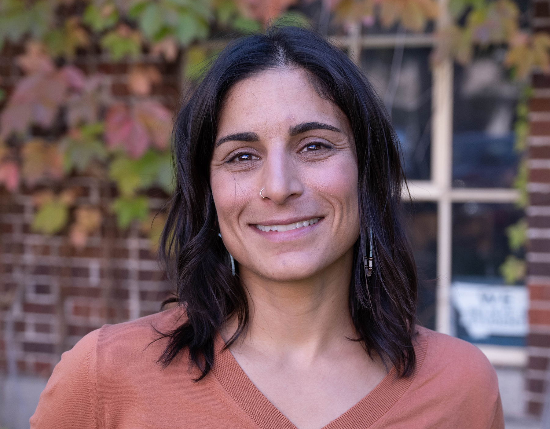 Woman with dark hair and wearing a salmon colored shirt smiles at camera.