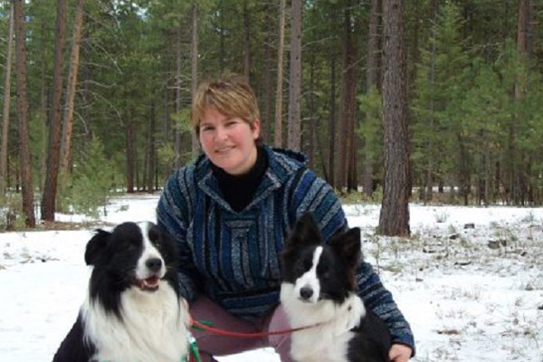 Woman crouches in the snow with two border collies